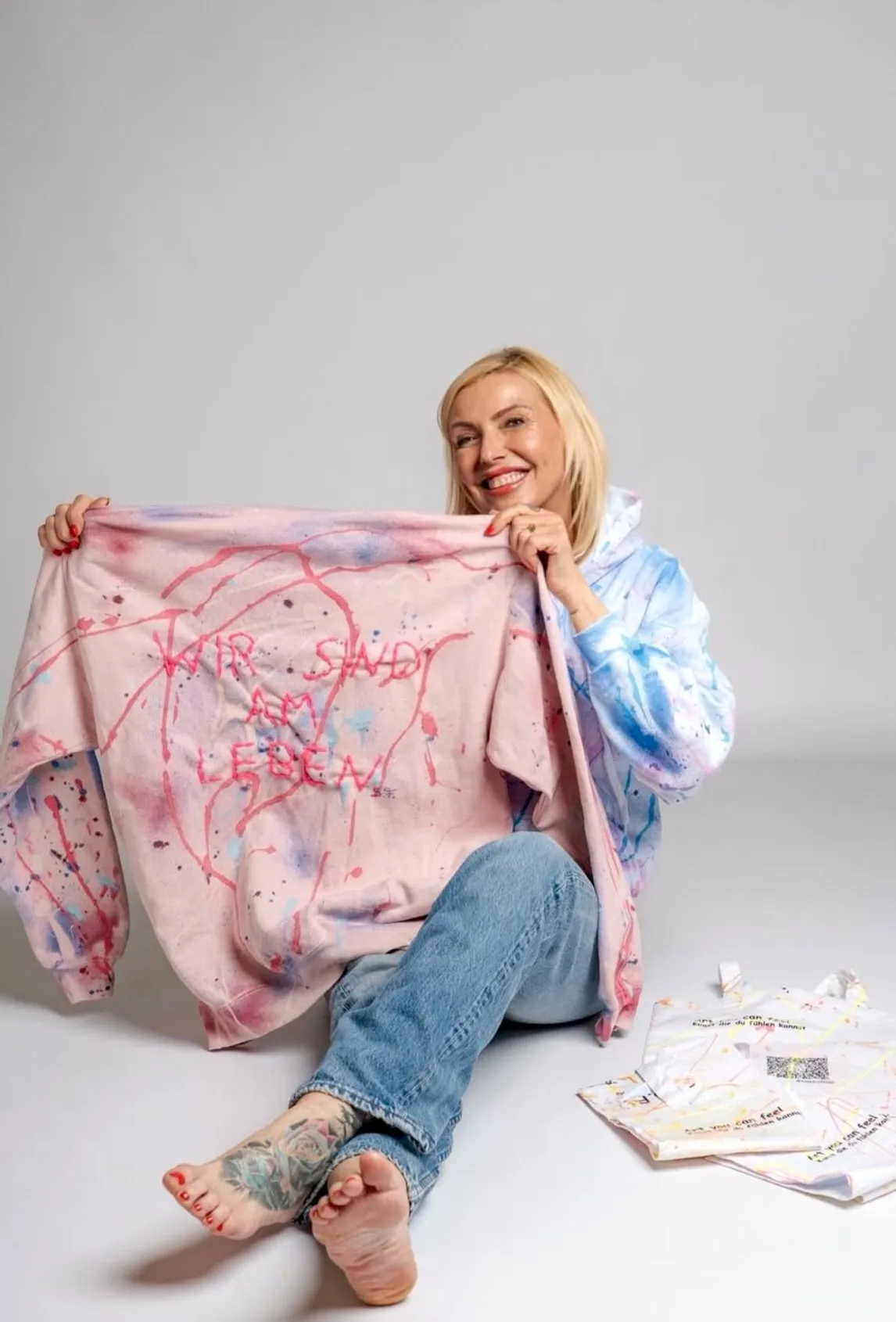 Suzy Forel mit einem handbemalten „Wir sind am Leben“-Unikat-Pullover im Atelier